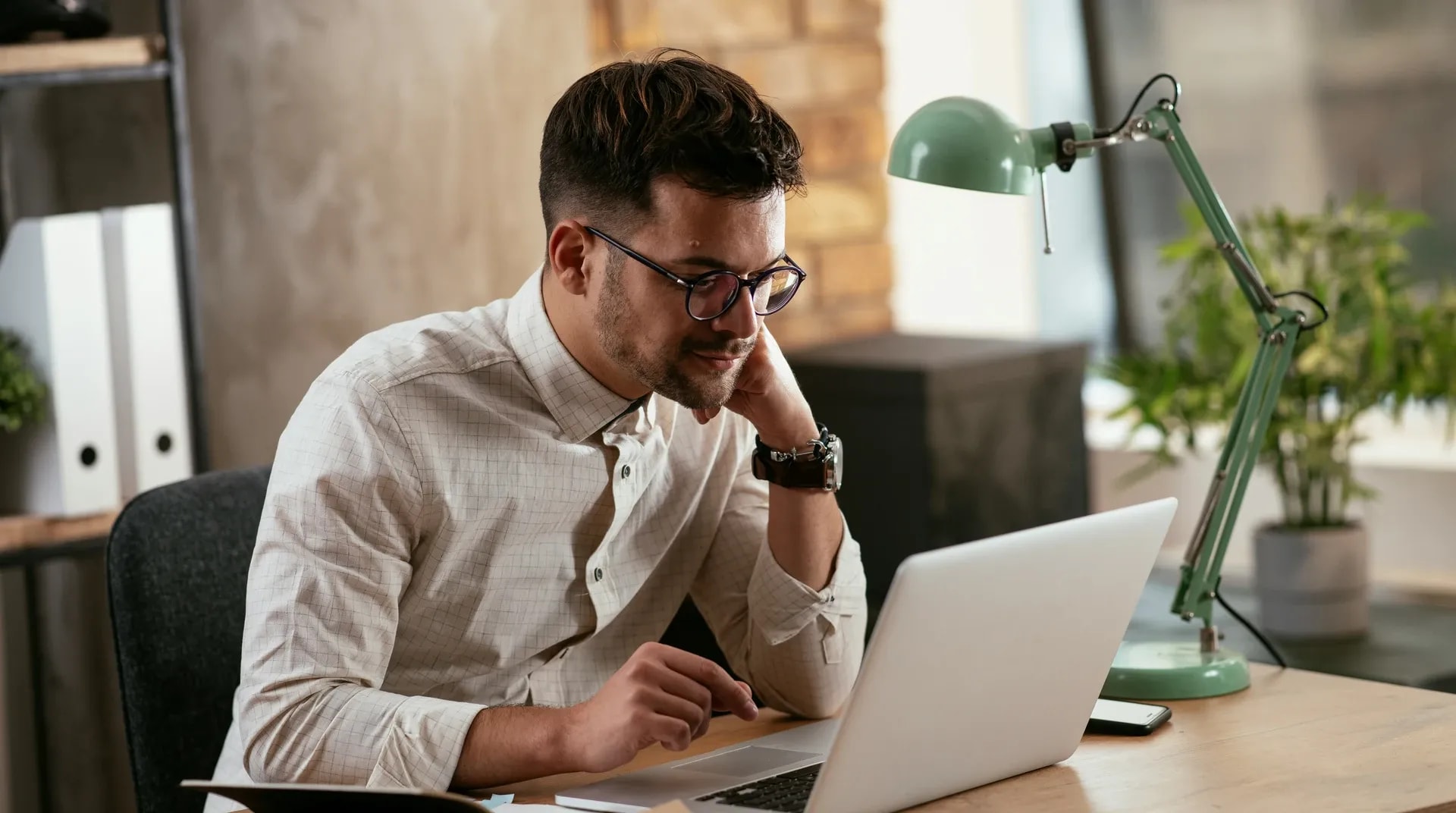 Iemand werkt geconcentreerd aan een laptop onder een bureaulamp