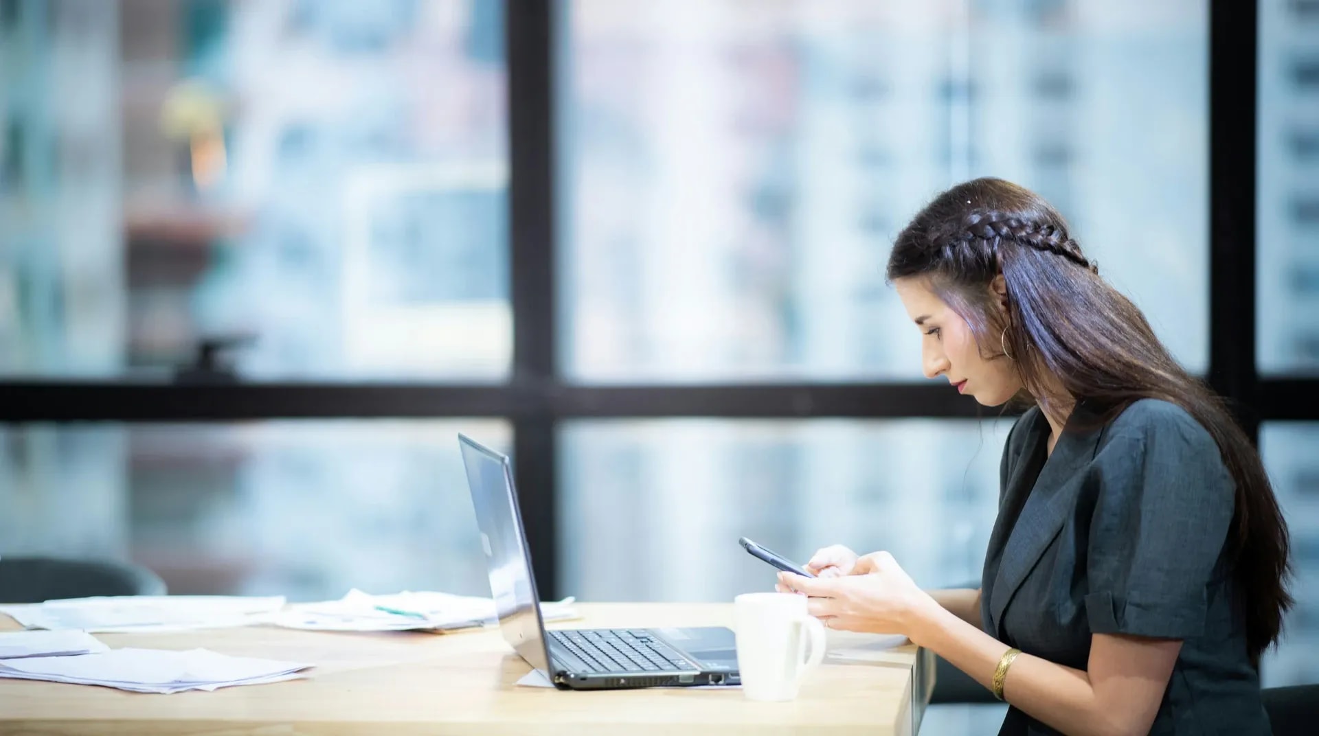 Iemand kijkt op de telefoon aan een bureau bij het raam